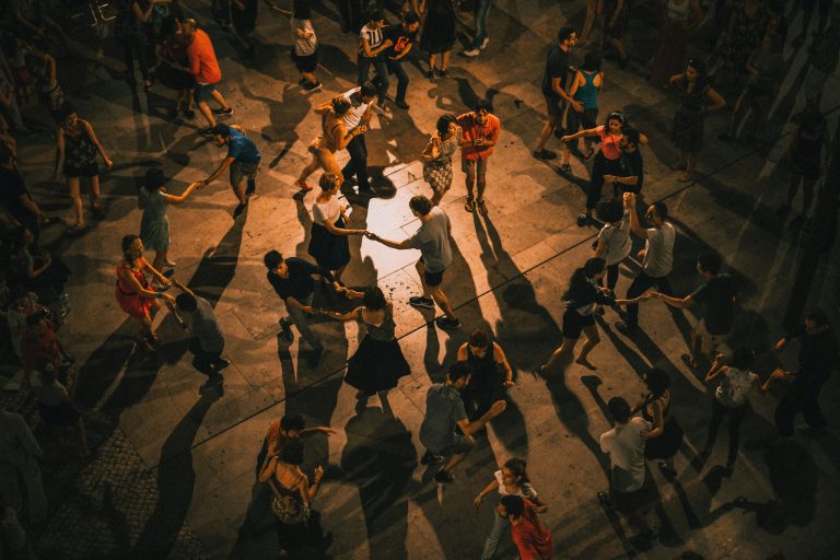 A top down view of a group of dancers performing on a wooden stage with atmospheric warm lighting casting shadows everywhere.