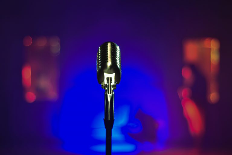 A music microphone sits center frame against a moody soft purple and orange lit background.