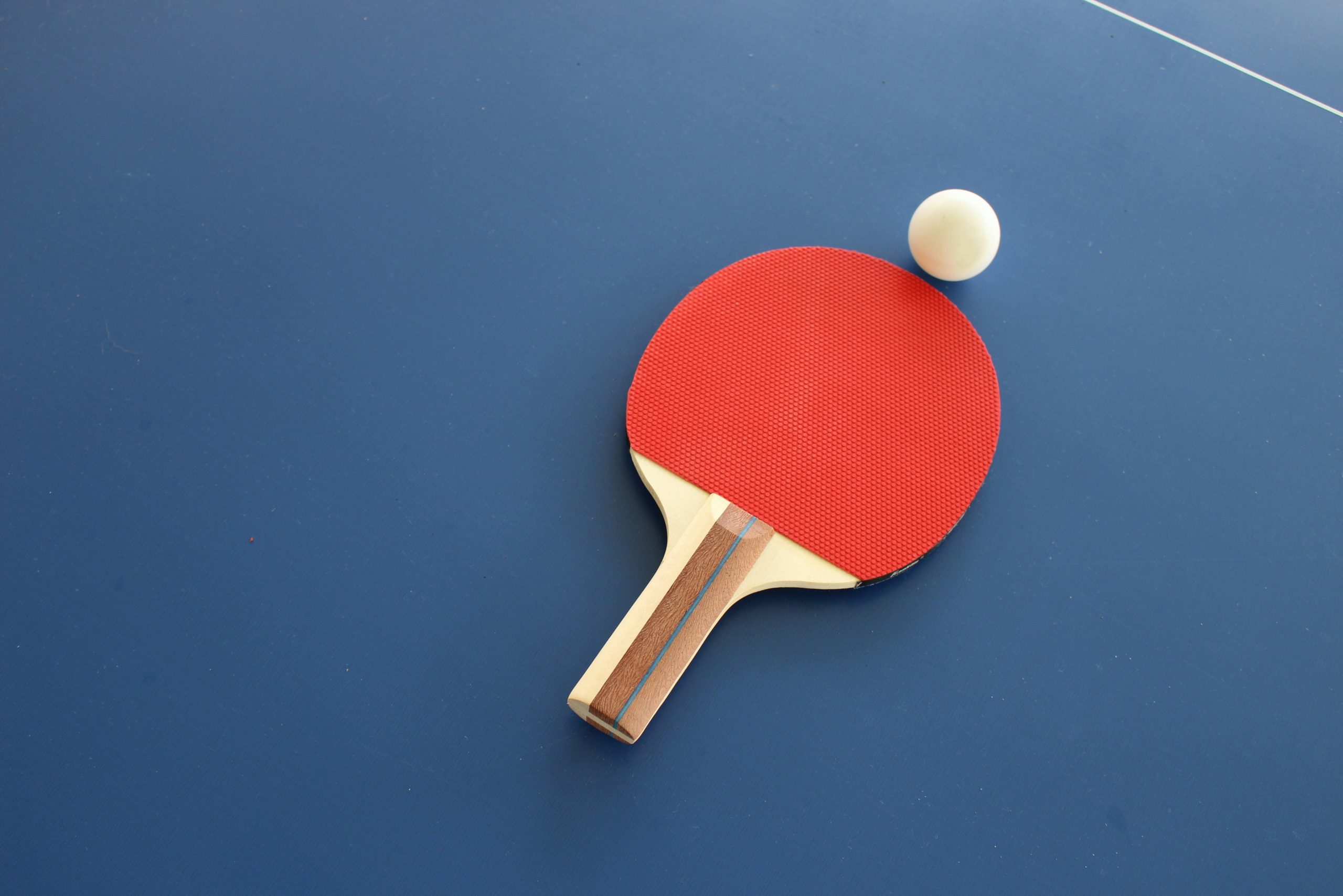 A table tennis paddle and ball sit together flat on a blue table.