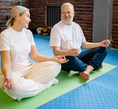 Two people sitting in a meditative pose on yoga mats smiling at each other.